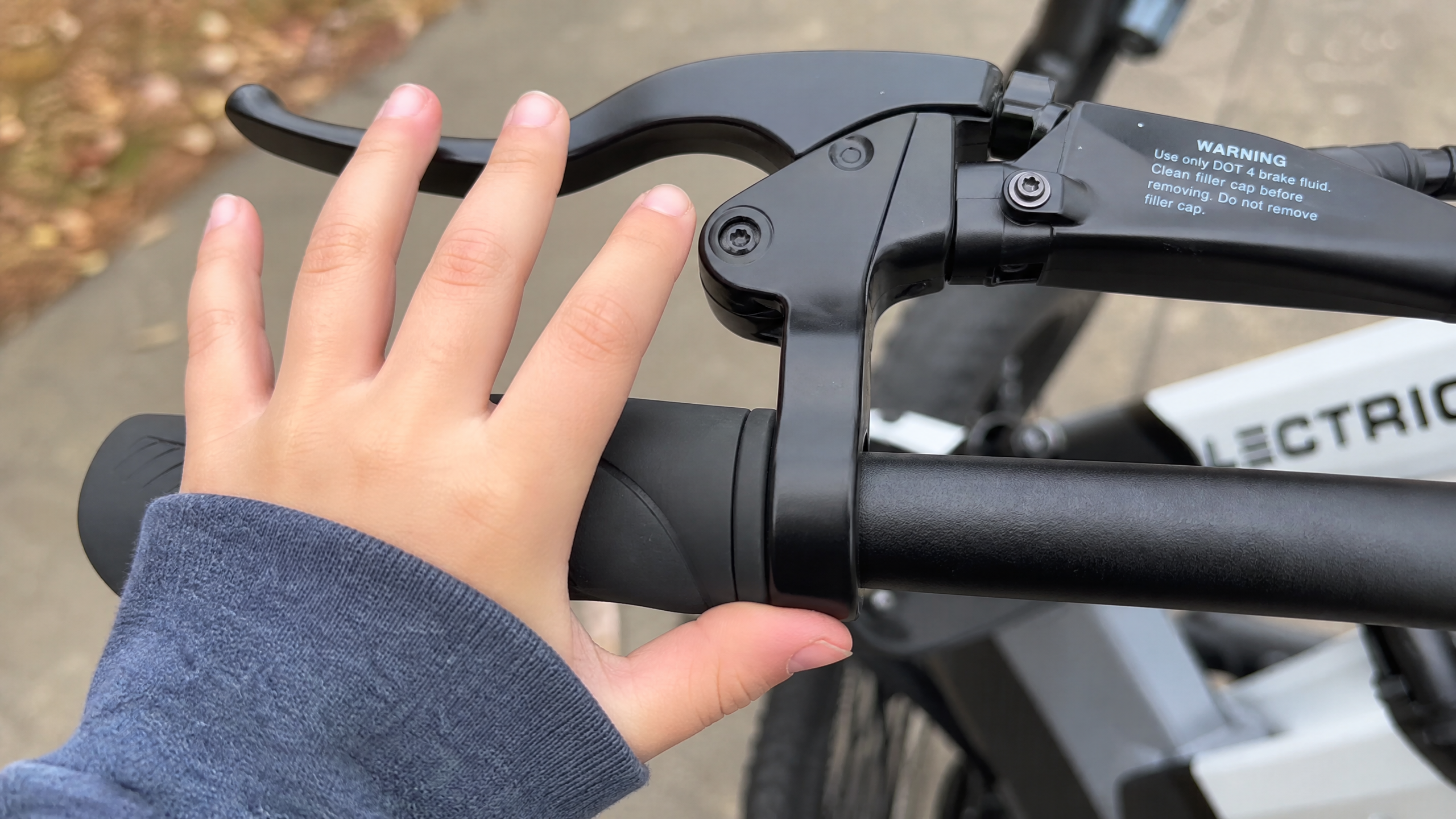 Close-up of a small hand struggling to reach and squeeze an electric bike's brake lever, highlighting the issue of brake levers not fitting small hands.