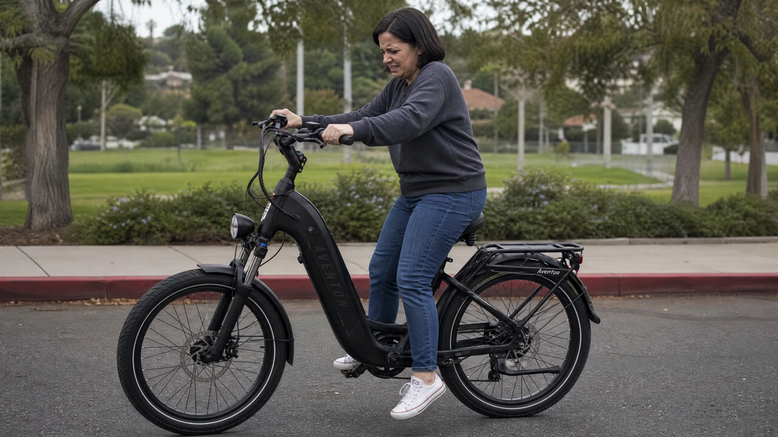 A short woman struggling to touch the ground with her feet while seated on an electric bike, illustrating a seat that won't go low enough.
