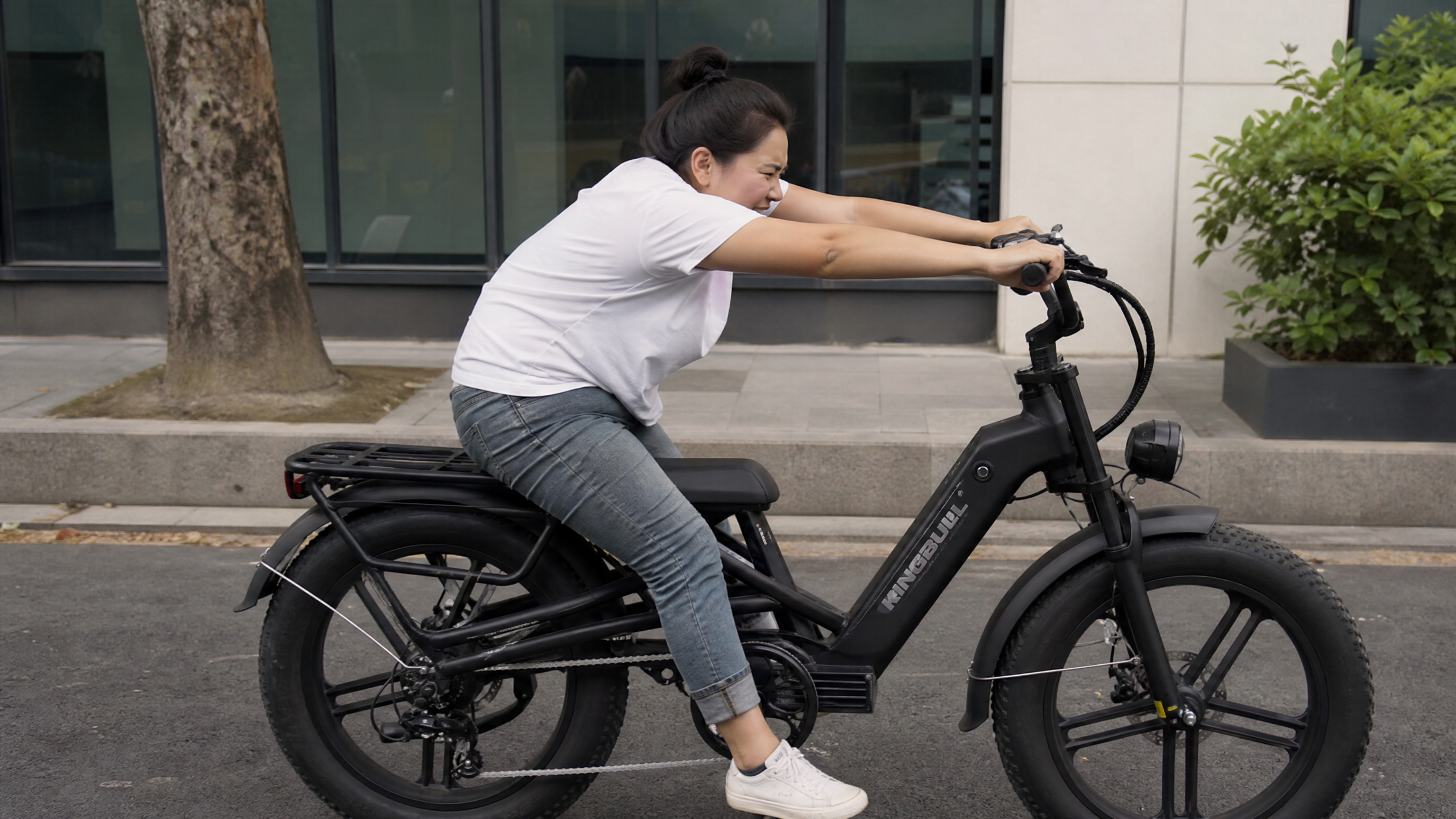A short woman on an electric bike, leaning forward and stretching her arms to reach the handlebars, showing discomfort and poor posture due to excessive reach.
